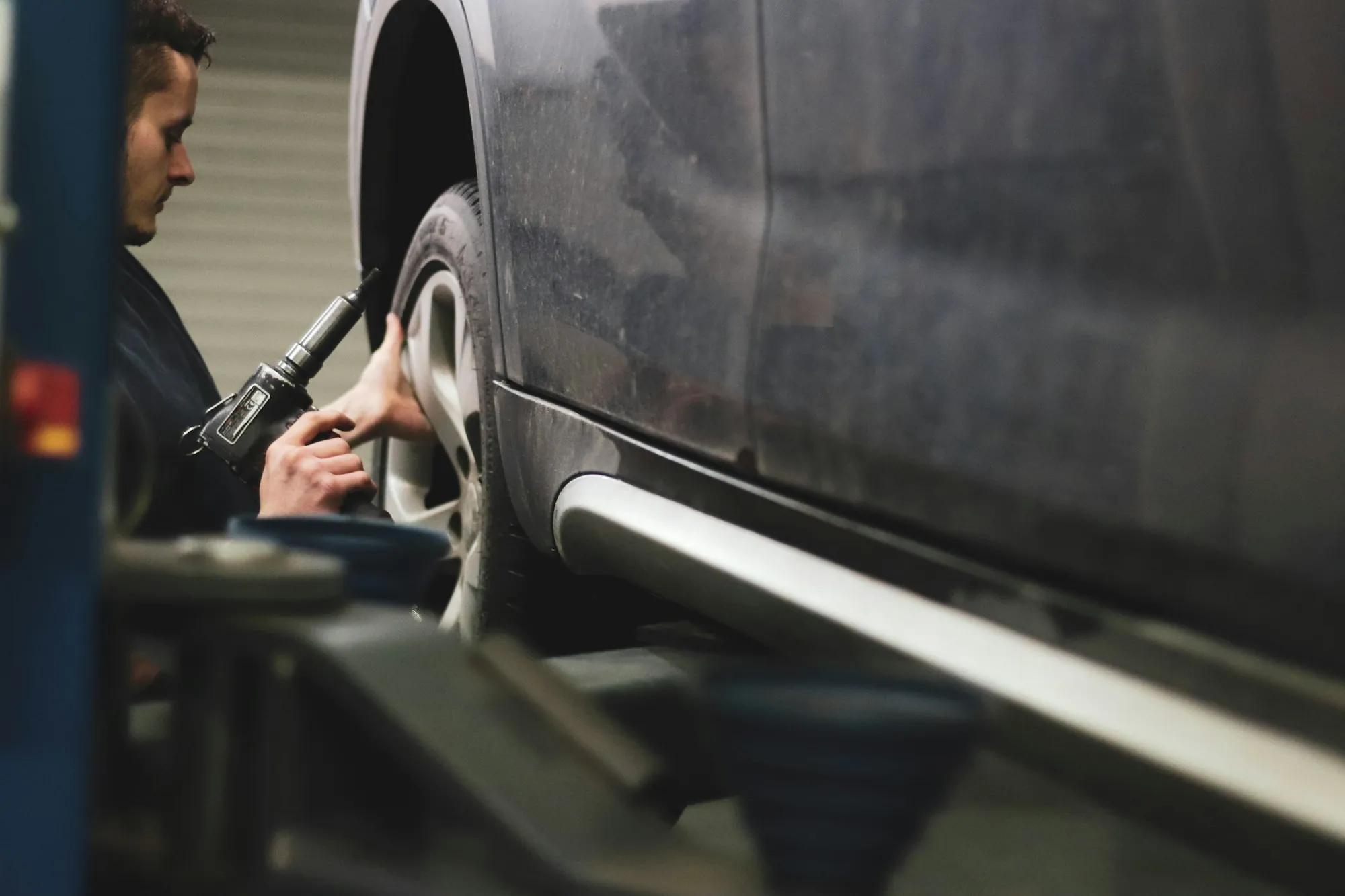Technician working at the wheel arch and lower door of a gray car